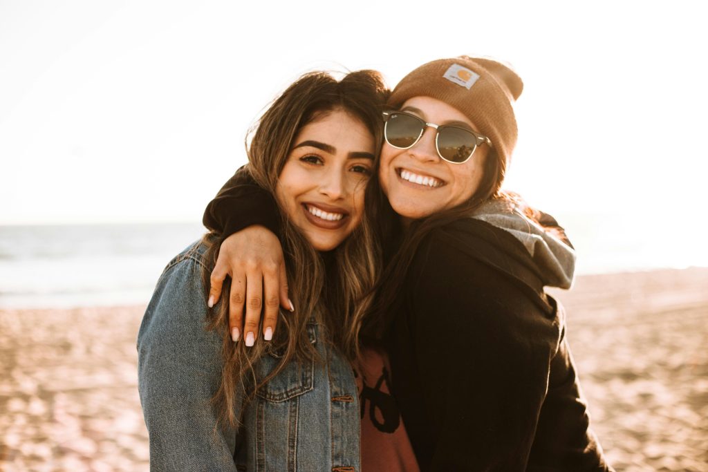 Two young women smiling and hugging on the beach, representing authentic Gen Z friendship and the joy of real-life connection.