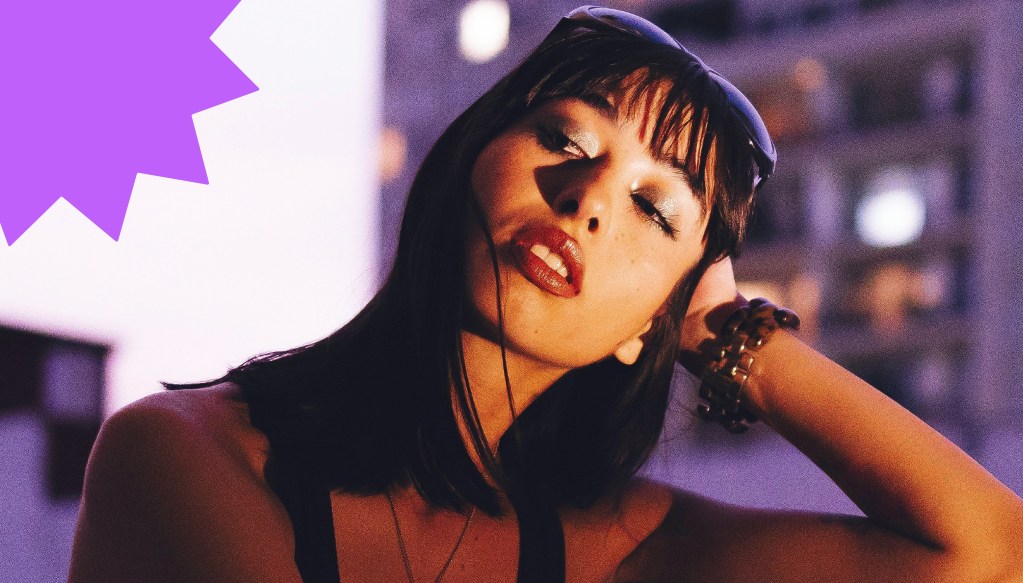 Jeune femme au coucher du soleil, expression pensive, avec des lumières urbaines floues en arrière-plan.