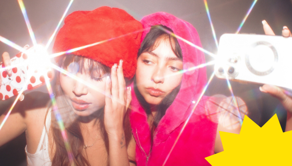 Deux amies prennent un selfie au flash, style Gen Z, avec des reflets colorés.