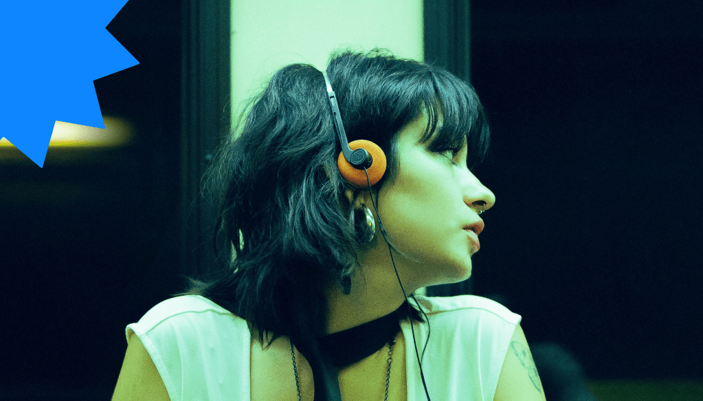 Chica con auriculares naranjas mira hacia la ventana de un vagón vacío, en silencio. La imagen evoca la soledad urbana tras un “dry texting”.